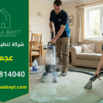 فريق عمل محترف من شركة تنظيف سجاد في عجمان، مكون من رجل وامرأة، يقوم بغسيل وتعقيم سجادة كبيرة بالبخار داخل غرفة معيشة منزلية، مع استخدام أغطية واقية للأرضيات.