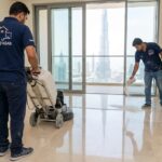 فريق عمل محترف من شركة جلي رخام في دبي يرتدي زي شركة "أحلى بيت" ويقوم بتلميع أرضيات شقة فاخرة باستخدام بودرة الكريستال وماكينات الجلي الحديثة مع إطلالة مباشرة على برج خليفة.